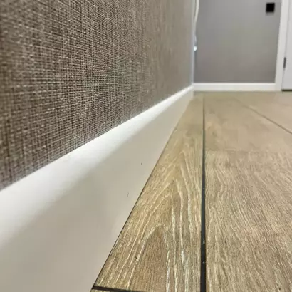 Современный белый плинтус на стыке стены с коричневыми текстурными обоями